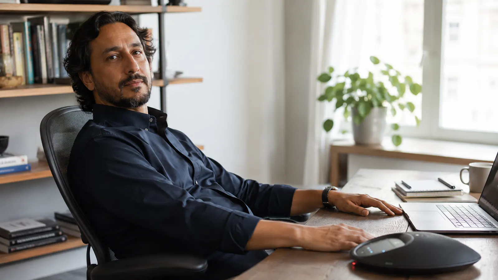 Remote worker sitting back relaxed with hands free while speaking on a speakerphone call, comfortable home office setting