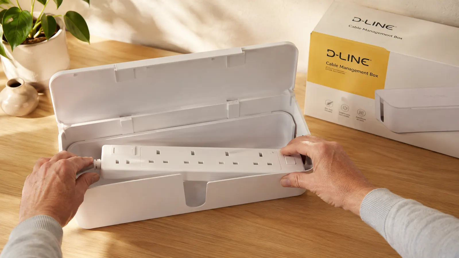 Hands placing a white power strip inside an open D-Line cable management box on a desk surface